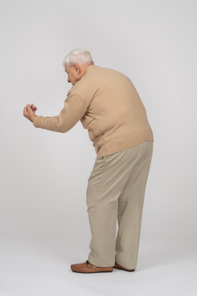 Rear view of an old man in casual clothes standing with outstretched arm and explaining something