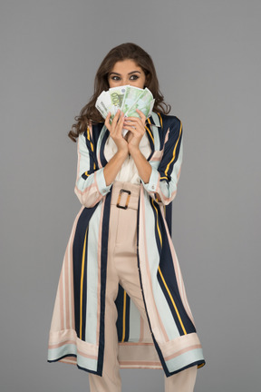 Cheerful middle-eastern woman covering her face with a fan made of banknotes