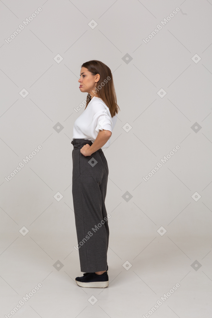 Вид сбоку недовольной молодой леди в офисной одежде, положившей руки на бедра