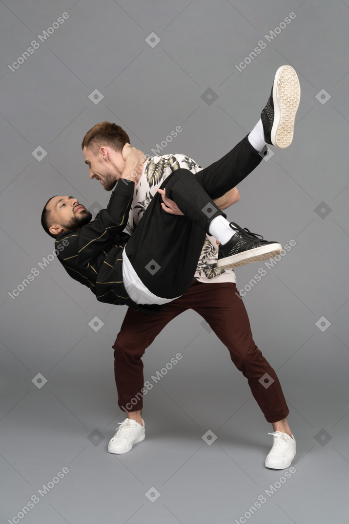 Young man leaning forward while holding another man bridal style