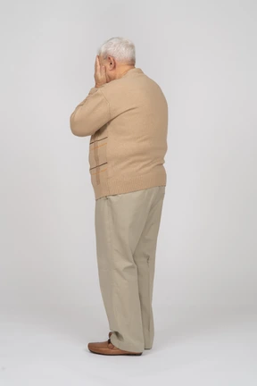 Side view of an old man in casual clothes covering face with hands