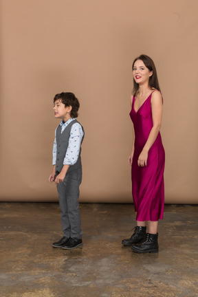 Femme en robe rouge regardant la caméra tandis que garçon debout près de