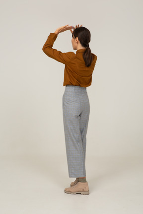 Vista posteriore di tre quarti di una giovane donna asiatica in calzoni e camicetta che alza le mani