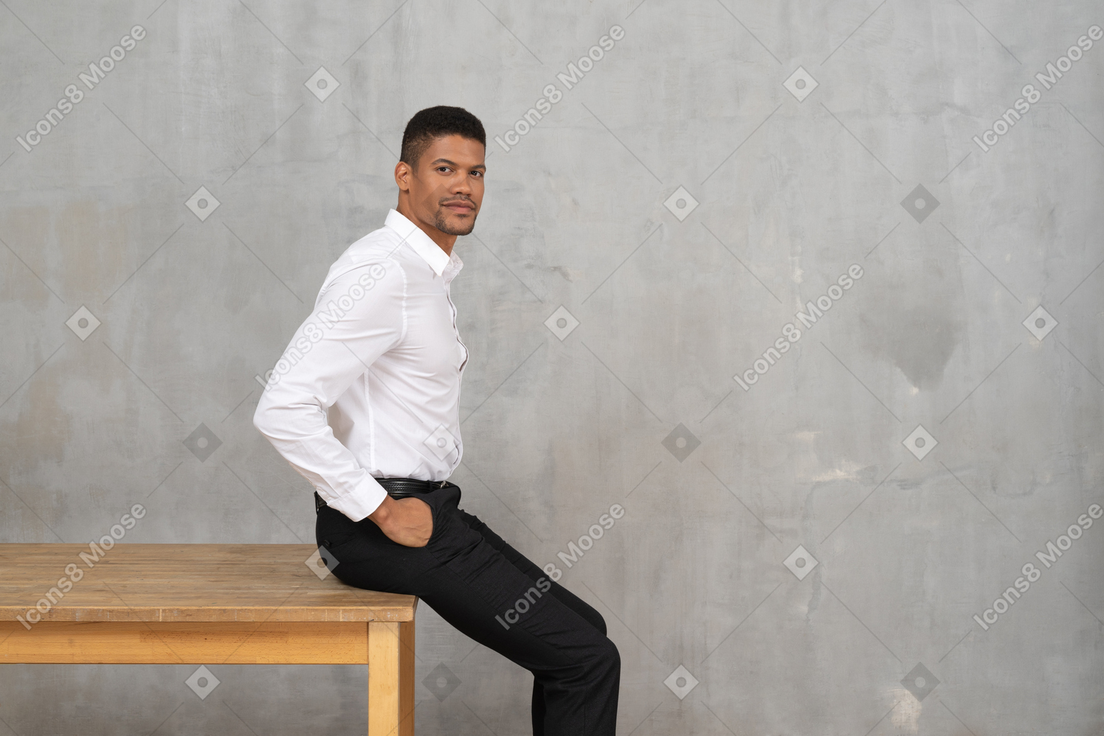 Мужчина в офисной одежде сидит на столе с руками в карманах