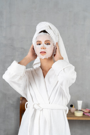 Woman in bathrobe with a face mask on holding her head
