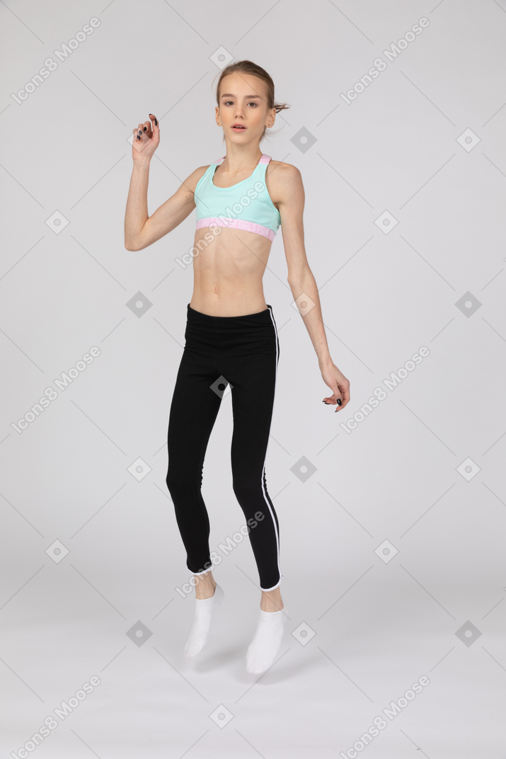 Vista de tres cuartos de una jovencita en ropa deportiva levantando la mano mientras salta