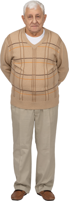 Vista frontal de un anciano con ropa informal de pie con las manos detrás de la espalda y mirando a la cámara