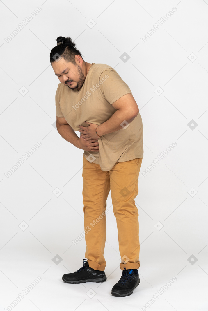 Plump asian man suffering from stomach pain and gripping his belly with both hands