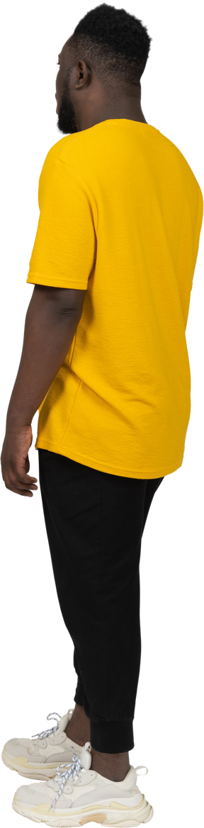 노란색 티셔츠를 입은 짙은 피부의 젊은 남자가 가만히 서 있는 모습
