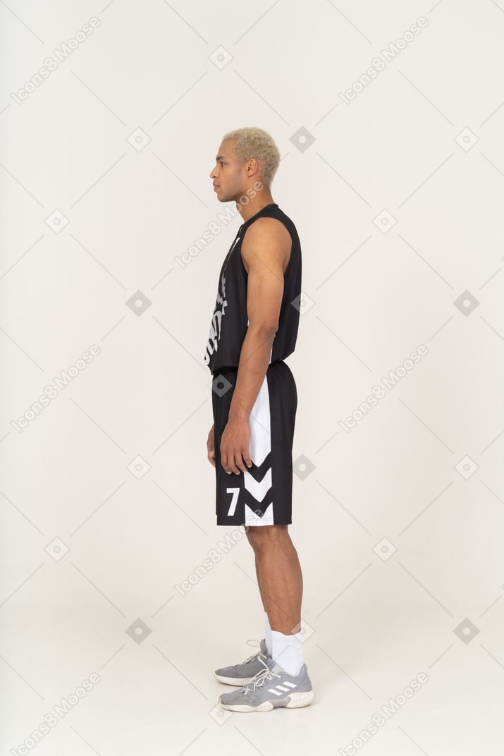 Vista laterale di un giovane giocatore di basket maschile in piedi immobile