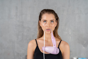 Front view of a young woman biting a hairdryer cord while looking fed up