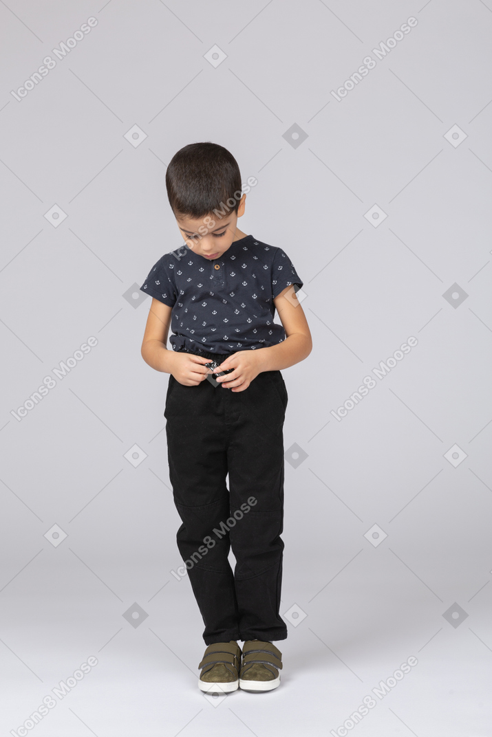 Vista frontal de um lindo garoto em roupas casuais olhando para as mãos