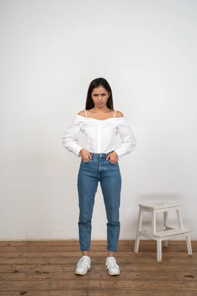 Woman with furrowed brows standing with hands in pockets