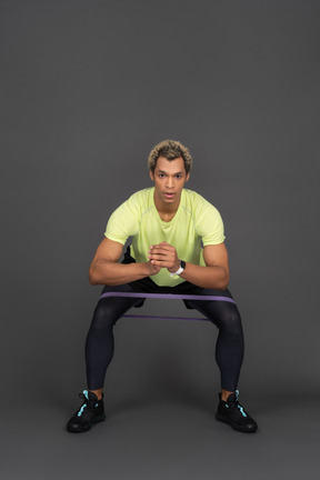 Front view of a dark-skinned young man squatting with an elastic rubber