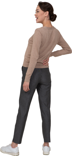 Vista posteriore di tre quarti di una donna che ride in pullover e pantaloni mettendo la mano sul fianco