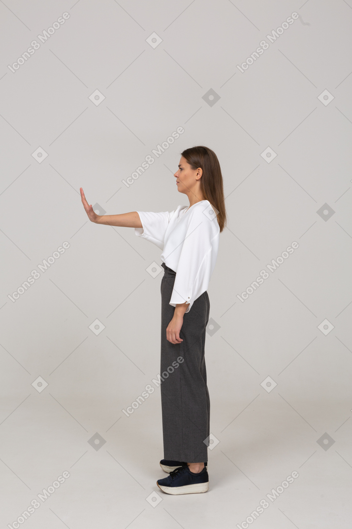 Вид сбоку недовольной молодой леди в офисной одежде, протягивающей руку