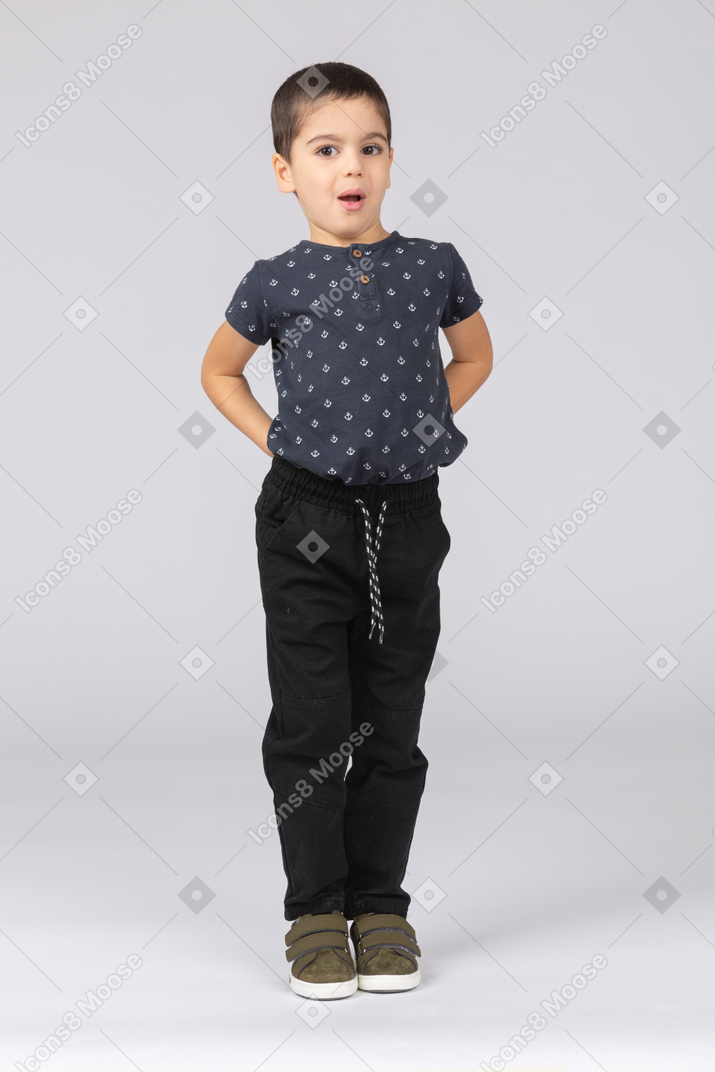 Vista frontal de um menino impressionado posando com as mãos nas costas