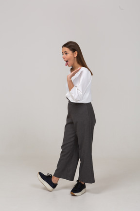Vista di tre quarti di una giovane donna in abiti da ufficio che mostra la lingua e alza la mano