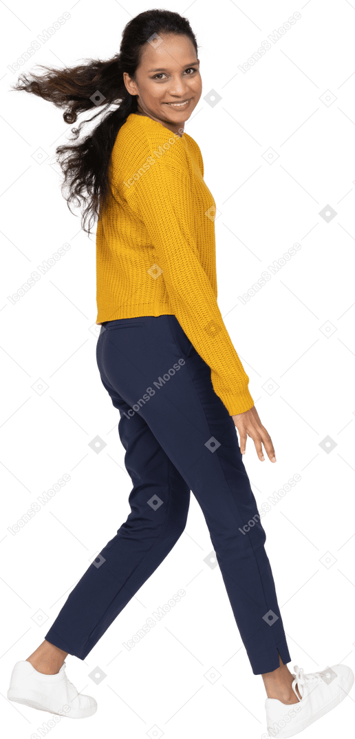 Side view of a happy girl in casual clothes walking and looking at camera