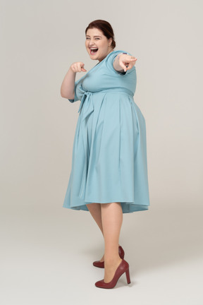 Vista frontal de uma mulher feliz em um vestido azul apontando com os dedos