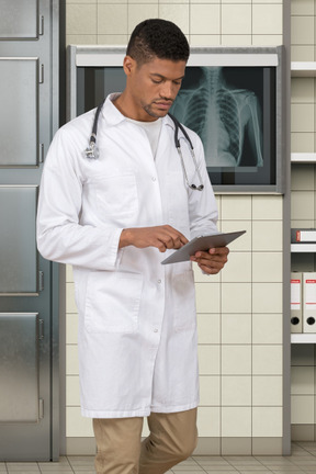 A male doctor in a white lab coat is looking at a tablet