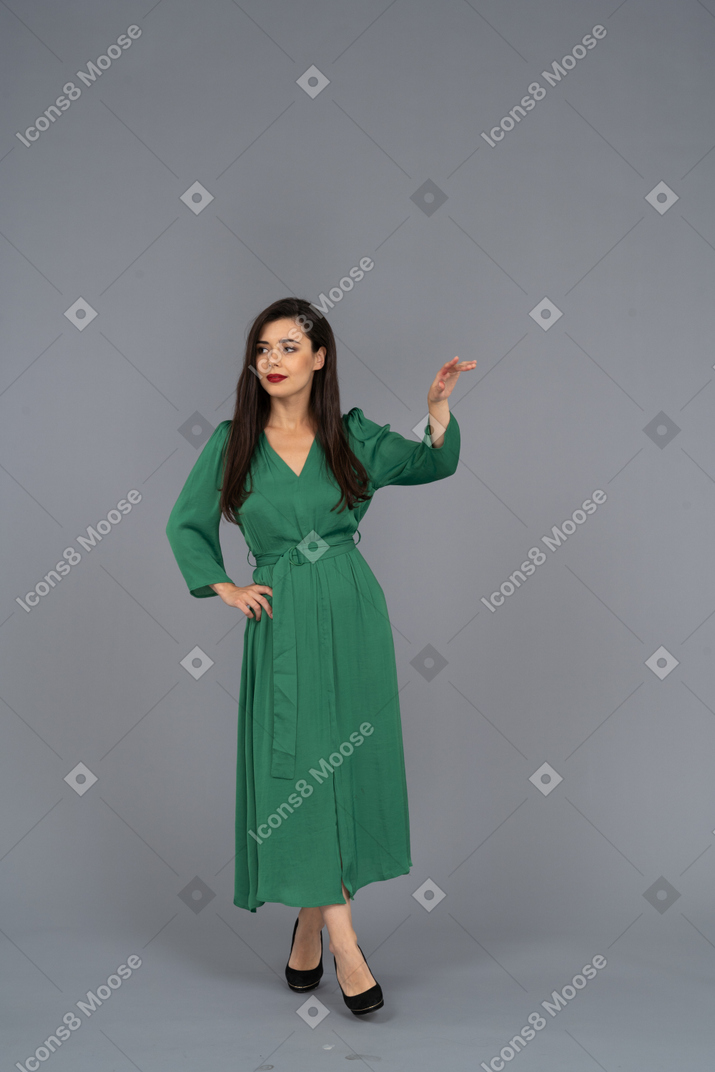 Vue de face d'une jeune femme en robe verte levant la main