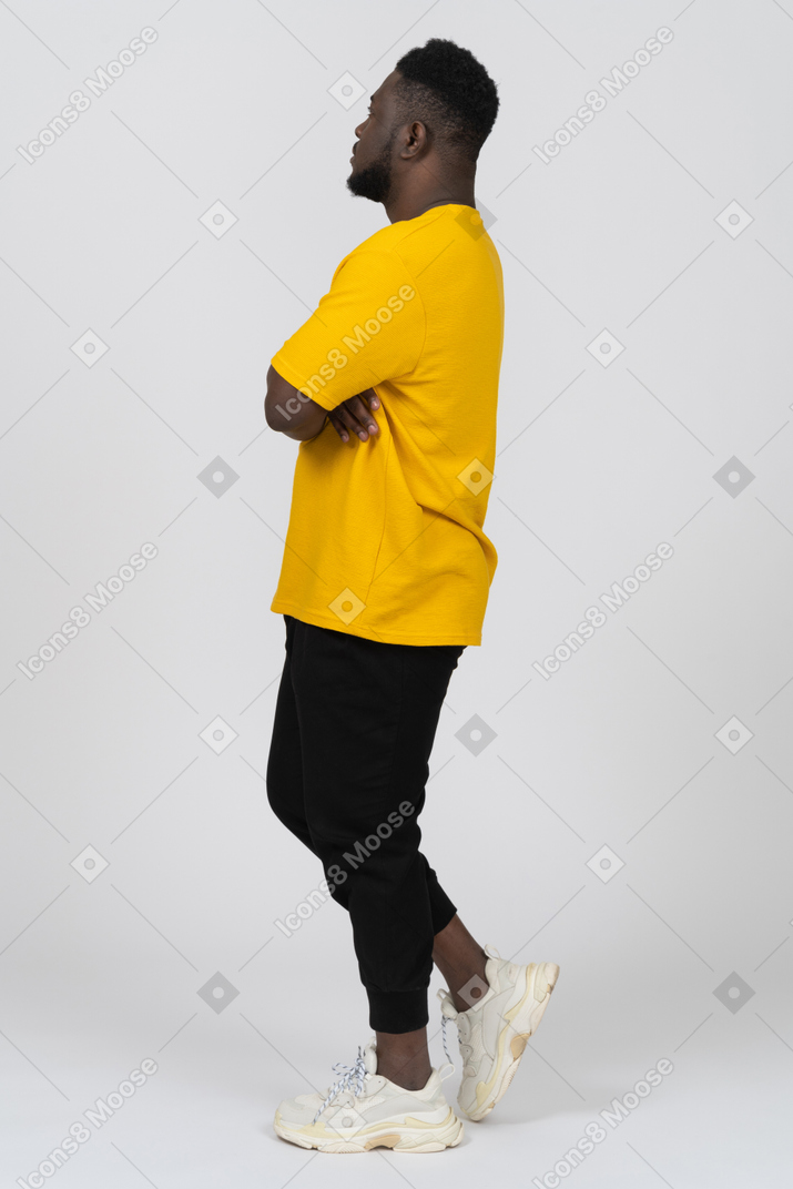 Вид сбоку на подозрительного молодого темнокожего мужчину в желтой футболке, скрестившего руки