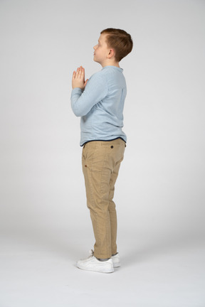 Вид сбоку милого мальчика, делающего молитвенный жест