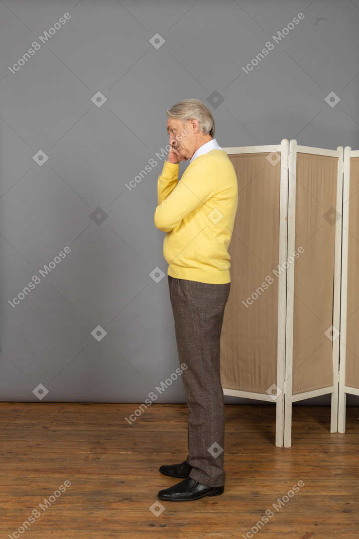Side view of a thoughtful old man touching chin near the screen