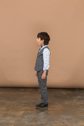 Vista laterale di un ragazzo in abito grigio che mostra la lingua
