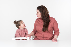 Мать и ее маленькая дочь, одетые в красную и розовую одежду, веселятся за обеденным столом