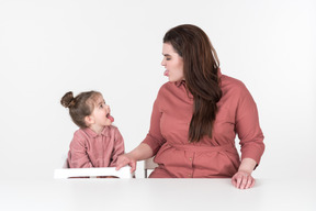 Mãe e sua filha, vestindo roupas vermelhas e rosa, se divertindo na mesa de jantar