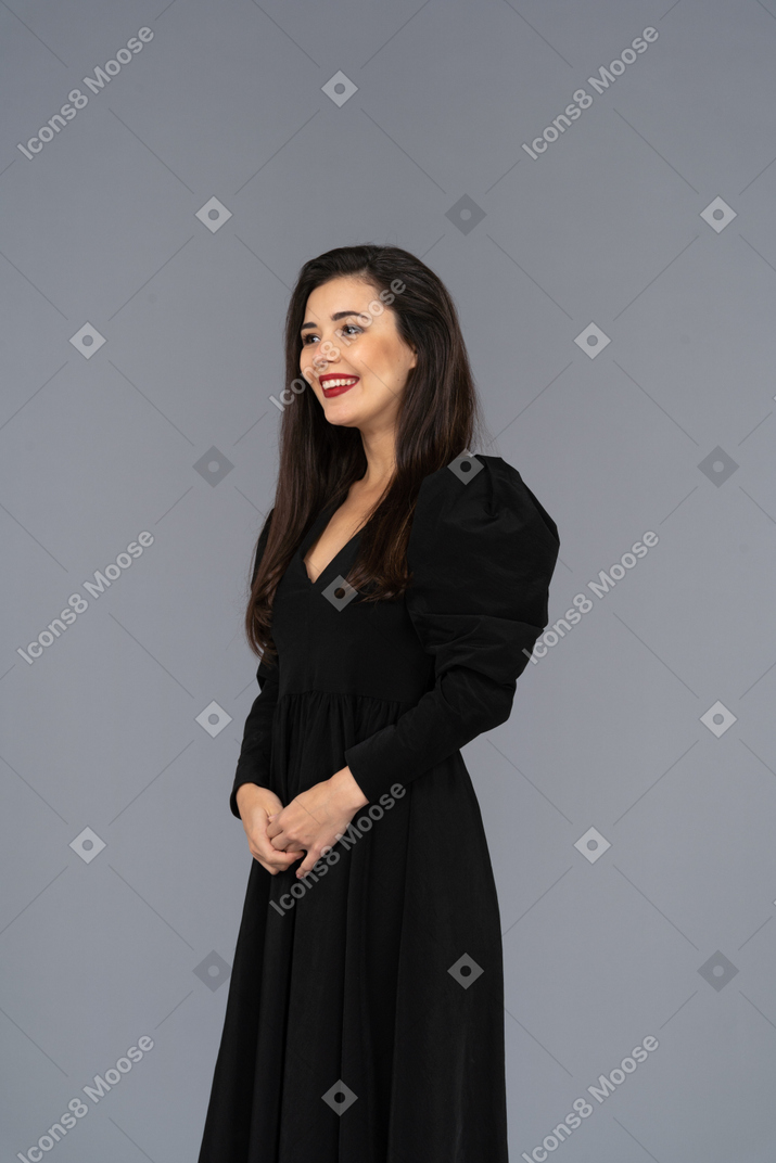 Three-quarter view of a smiling young lady in a black dress standing still