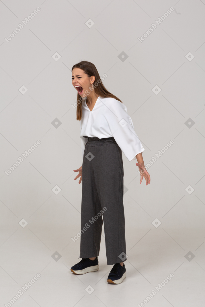 Vista di tre quarti di una giovane donna che urla pazza in abiti da ufficio allargando le mani