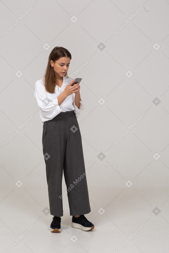 Front view of a young lady in office clothing checking feed via phone