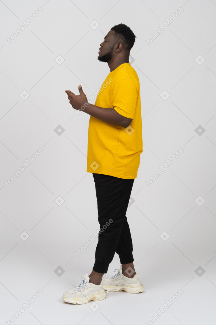 노란 티셔츠를 입은 사려깊은 몸짓을 하는 짙은 피부의 젊은 남자의 측면