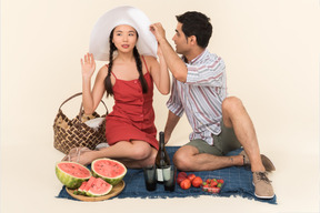 Interracial couple having picnic and man adjusting girl's hat