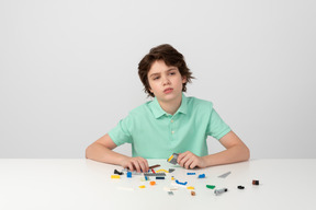 Thoughtful boy in green polo shirt playing with building blocks