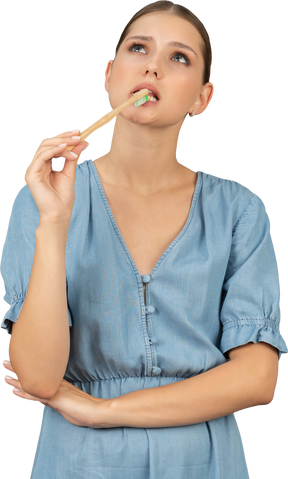 Vista frontal de uma jovem de vestido azul escovando os dentes