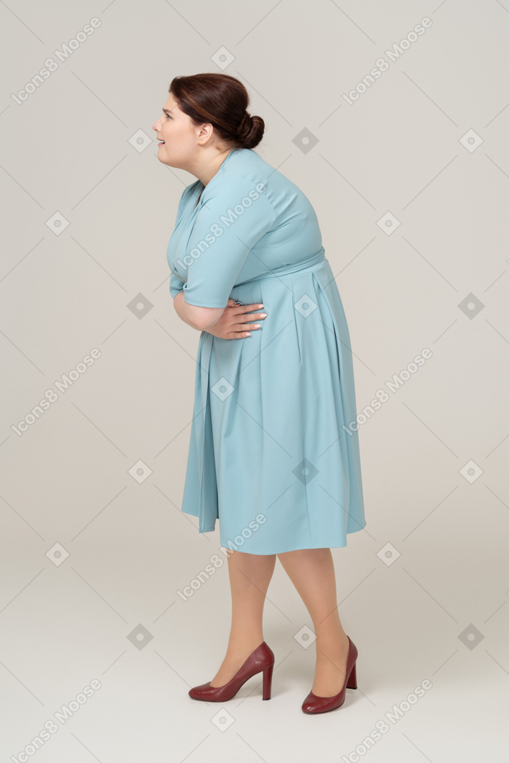 Вид сбоку на женщину в синем платье, страдающую от боли в животе