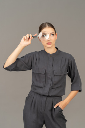 Front view of a young woman in a jumpsuit holding a magnifying glass