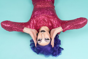 Drag queen in pink dress lying on the floor & holding their face