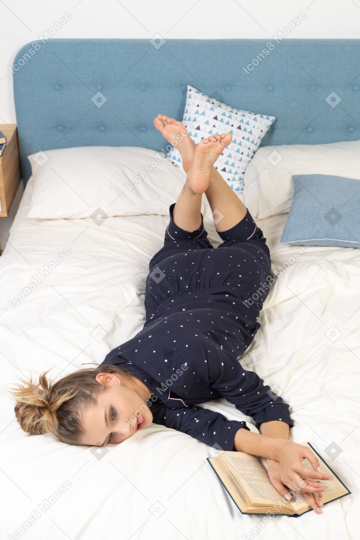 一本无聊的年轻女性在床上看书的前视图