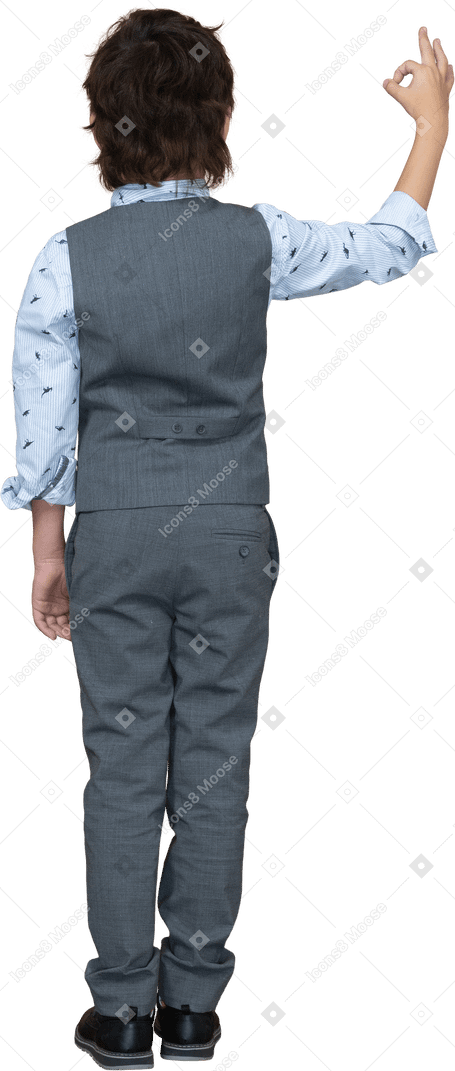 Vista trasera de un niño con traje gris que muestra el signo de ok