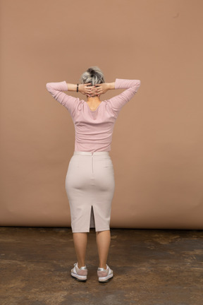 Rear view of a woman in casual clothes standing with hands behind head