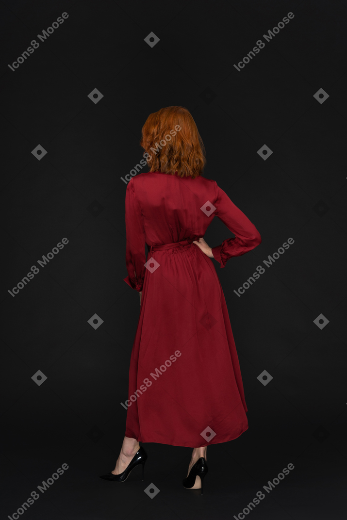 Young woman in red dress standing back to camera with hand on hip