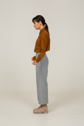 Vista laterale di una giovane donna asiatica in calzoni e camicetta che stringe i pugni