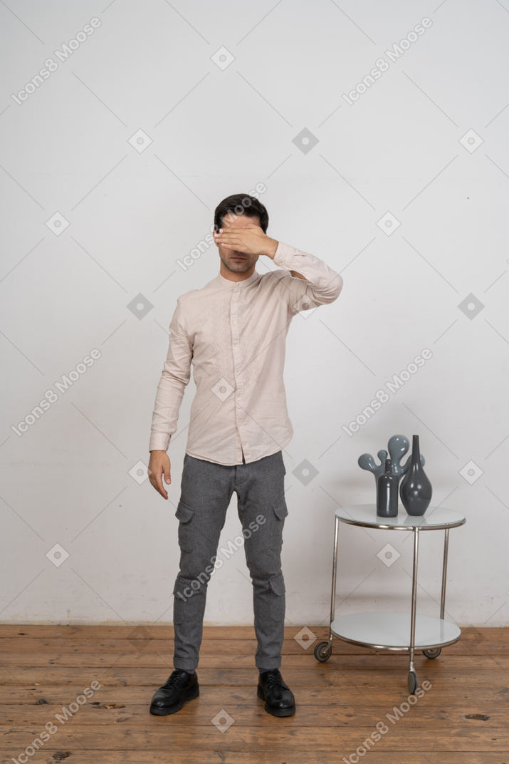 Вид спереди человека в повседневной одежде, закрывающего глаза рукой