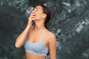 Close-up laughing woman in sports bra hiding her mouth