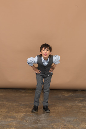 Vista frontal de um menino de terno em pé com as mãos nos quadris e curvando-se